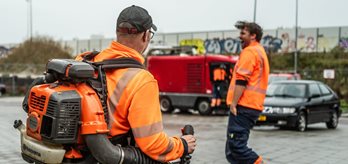 Twee lachende medewerkers van Gemeente Groningen die een parkeergelegenheid schoon maken met bladblazers