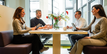 Vier medewerkers in overleg zittend aan tafel