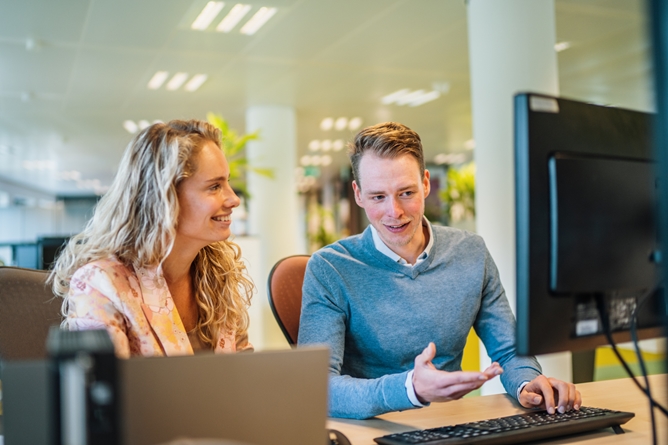 Twee medewerkers achter een bureau kijkend naar een computerscherm
