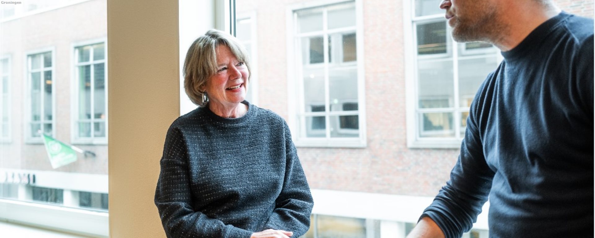 Twee collegas met elkaar in gesprek zittend bij een raam 3