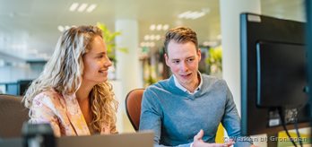 Twee medewerkers achter een bureau kijkend naar een computer