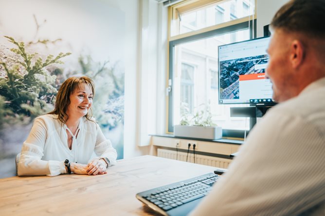 Twee medewerkers in overleg aan een tafel met een TV scherm 2