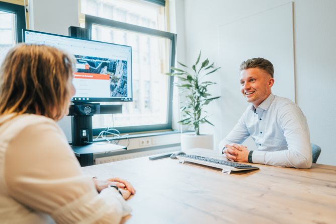 Twee medewerkers in overleg aan een tafel met een TV scherm