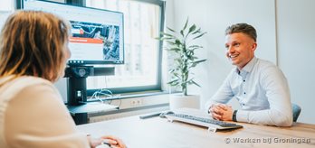 Twee medewerkers in overleg aan een tafel met een TV scherm